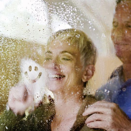 Un couple souriant regarde à travers une fenêtre humide